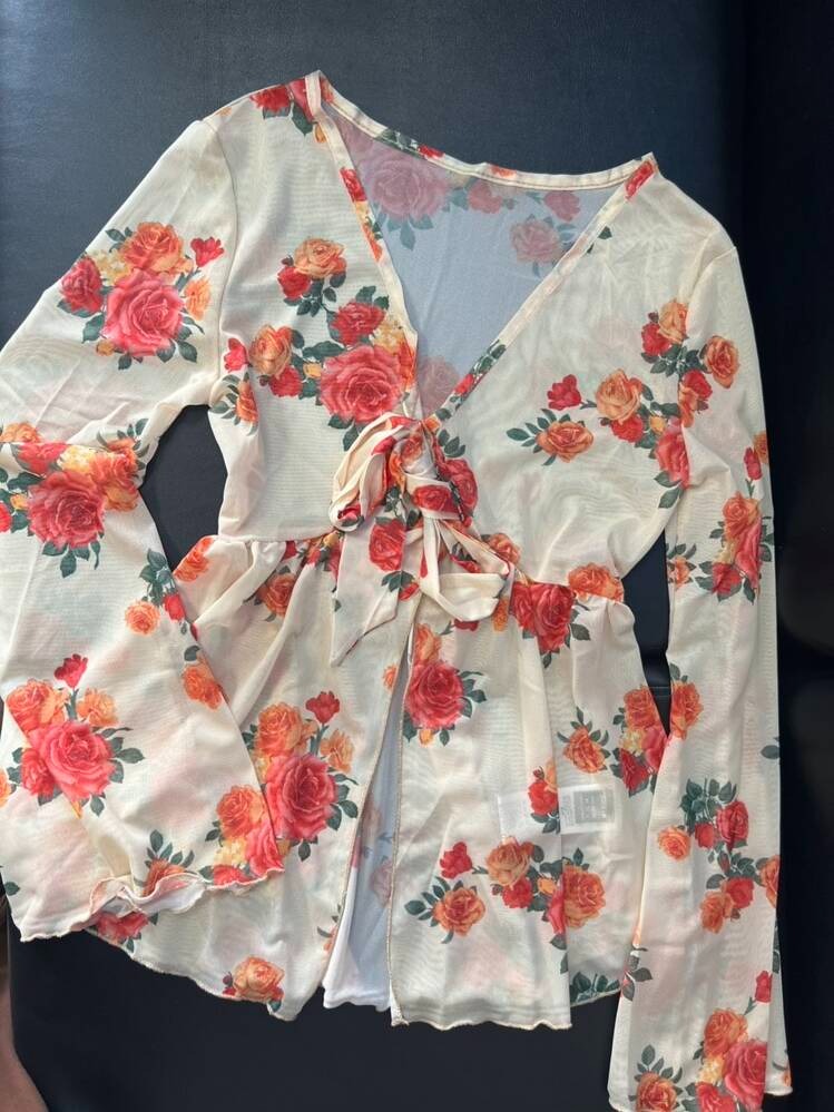 เสื้อสีชมพูวินเทจลายหนังสือพิมพ์และกุหลาบแขนยาว คอวีผูกโบว์ จัดแสดงอยู่บนหุ่นโชว์ เข้ากับกระเป๋าสะพายข้างสีเงินและสร้อยคอลูกปัดรูปดาวทะเล